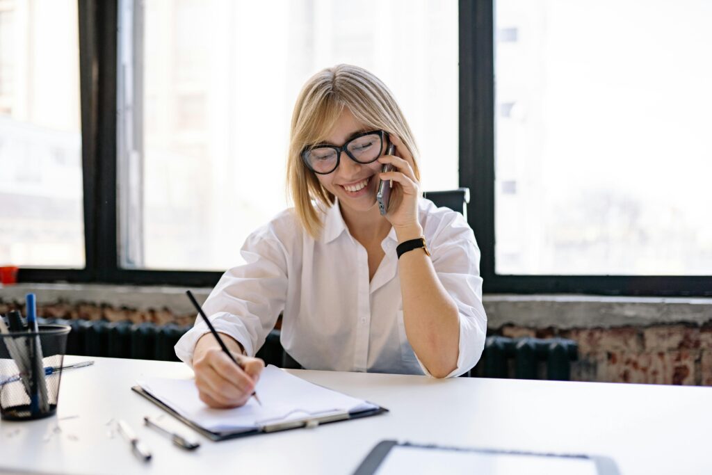 Performance marketing director key skills summary being written by a person in a white shirt, sitting at a desk with a notebook and pen, in a bright office with large windows.
