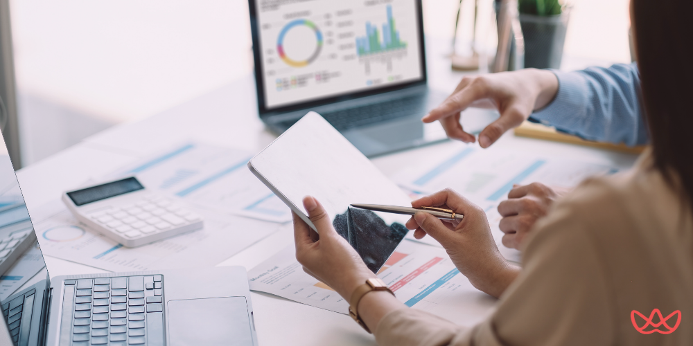 Two professionals collaborating at a desk with digital tools, printed documents, and a calculator, emphasizing the review of an Account Manager Resume Template.
