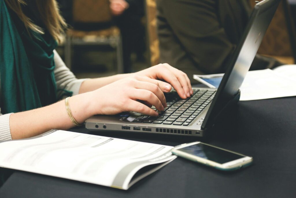 Person typing on a laptop next to a resume draft and smartphone, working on a Copywriter Resume Template.