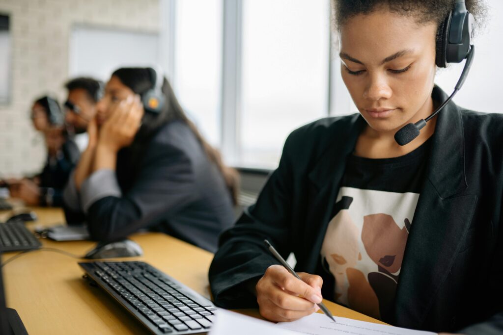 Focused professional with a headset taking notes in a modern office, representing the dedication and detail-oriented skills showcased in a Customer Relationship Manager (CRM) Resume Template.