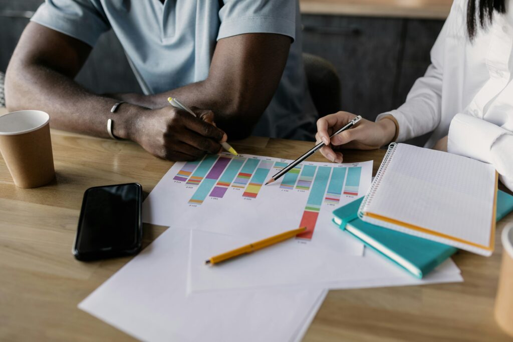 Two professionals reviewing colorful bar charts and notes at a wooden desk, possibly discussing a Digital Marketing Consultant Resume Template layout.