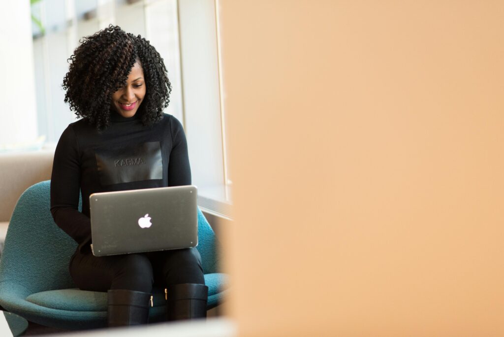 Woman smiling while working on her laptop, designing an Email Marketing Copywriter Resume Template.