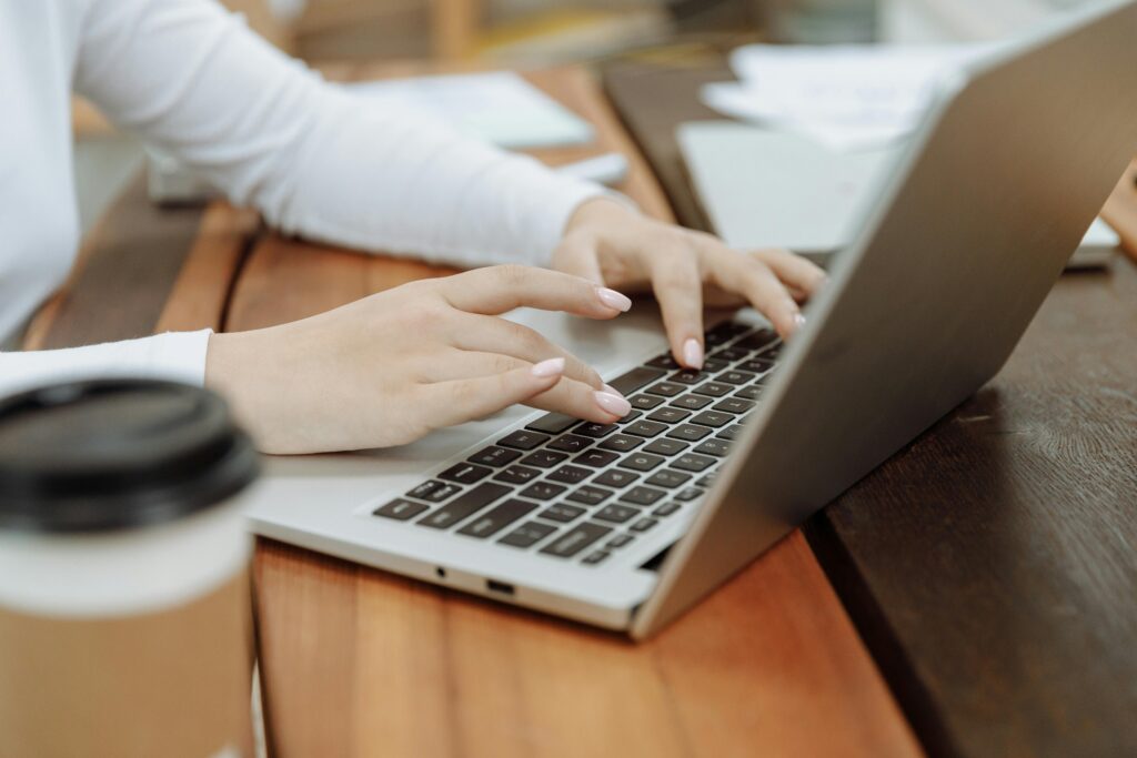 Hands typing on a laptop keyboard with a coffee cup nearby, working on a Digital Product Designer Resume Template.