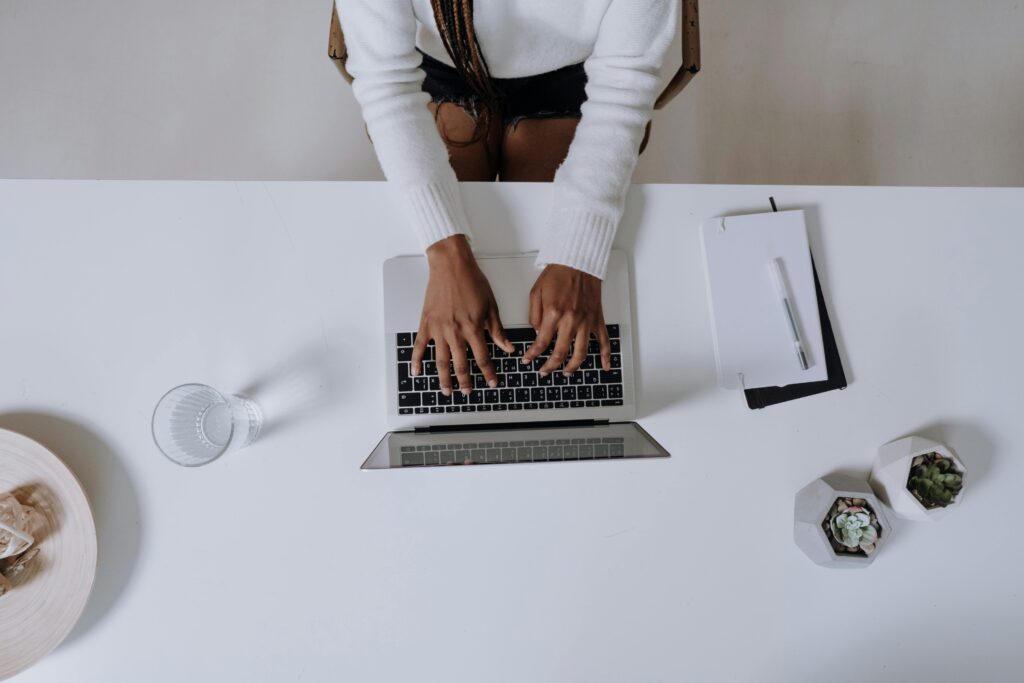 Hands typing on a laptop over a white desk, representing the efficiency of Why to Outsource SEO?