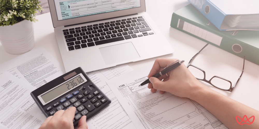 A person's hands using a calculator and filling out tax forms (likely a U.S. Corporation Income Tax Return - Form 1120), with a laptop, eyeglasses, and binders on a desk. The image also contains the text "Healthcare Accounting Services."