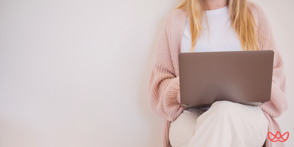 A person with long blonde hair, wearing a white shirt and a pink cardigan, sitting and working on a laptop. The image also contains the text "Overseas Payroll Services & Outsourcing in Latin America."