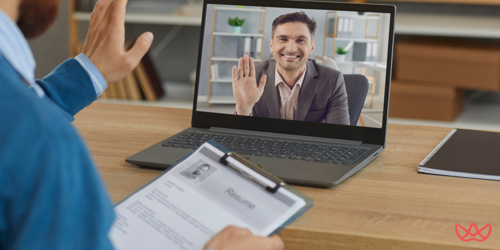 A man holding a resume during a virtual job interview with another man on a laptop screen, who is waving. The screen also displays the text "Top Temp Agencies & Remote Customer Service Jobs Near You in 2025."