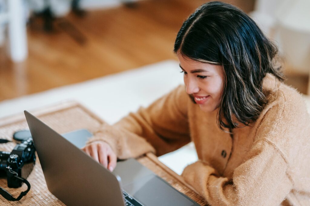 Smiling woman working on laptop researching SEO outsourcing for agencies from home office.