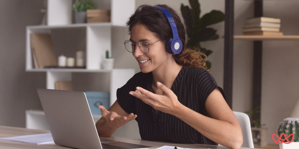 A woman with curly brown hair and glasses, wearing blue headphones and a striped shirt, smiling and gesturing with her hands while looking at a laptop, suggesting a video conference or virtual interview. The image also contains the text "Top Software Engineer Staffing Agencies for Your Hiring Needs in 2025."