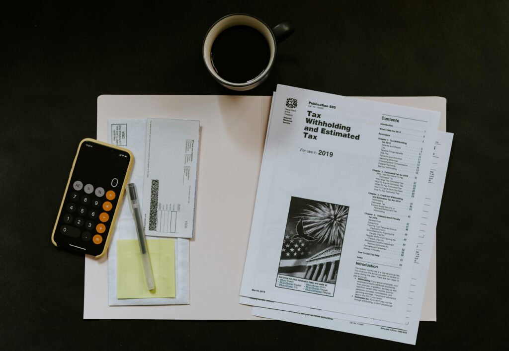 A close-up of a desk with financial documents, a calculator being used, eyeglasses, and a laptop displaying a financial chart with bar graphs, suggesting detailed financial analysis. The image also contains the text "Outsourced Financial Controller Everything You Need to Know."