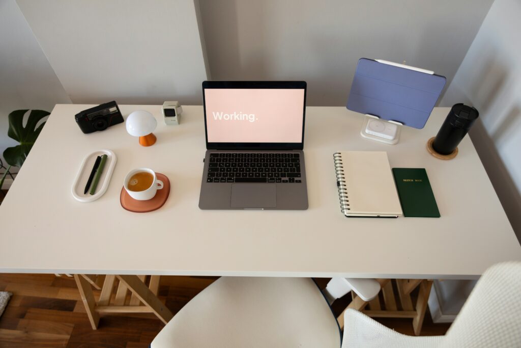 An overhead shot of a person's hands on a laptop keyboard and touchpad, with a smartphone, notebook, and stack of books on a desk, suggesting a workspace for managing finances or business operations.