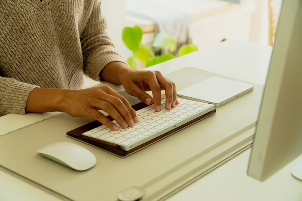 Close-up of hands typing on a modern white keyboard with a wooden base, next to a white mouse and a computer monitor, suggesting productive work often found in settings relevant to top CFO executive search firms.