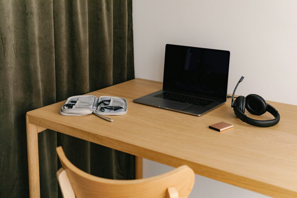A tidy wooden desk with an open laptop, a pair of black over-ear headphones, a small rose gold object, and an open tech organizer case. This organized workspace is indicative of the efficient environment of a top product management recruitment agency.